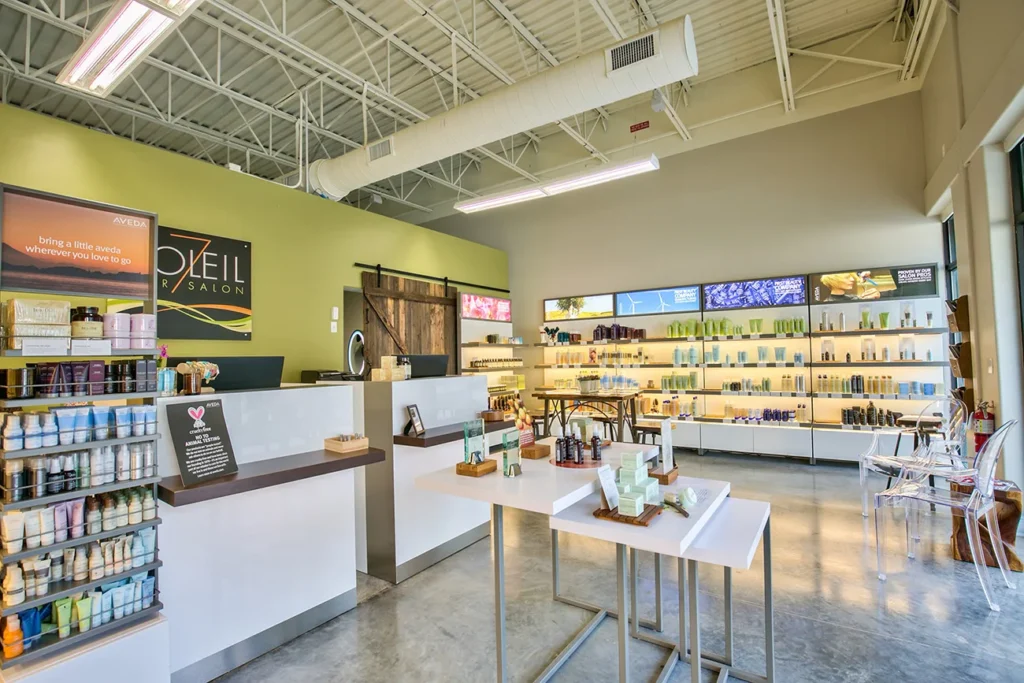 Modern salon interior with product displays, two central tables with skincare items, reception desk, shelves of beauty products, and bright natural lighting from large windows. - Soleil 7 Hair Salon in Tallahassee, FL