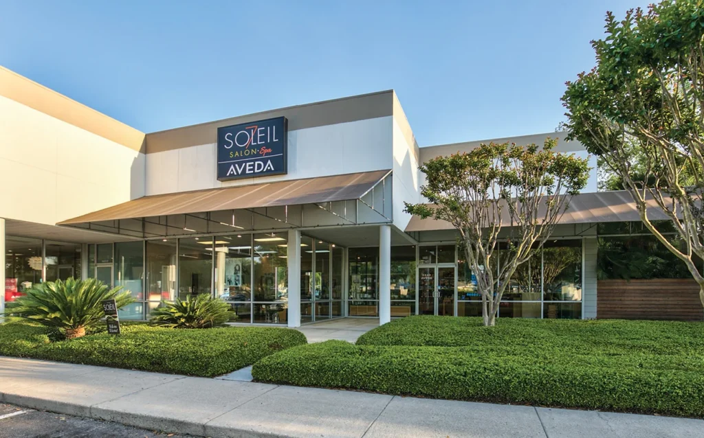 Exterior view of Soleil Salon & Spa Aveda, showing a modern building with large windows, landscaped greenery, and clear signage above the entrance. - Soleil 7 Hair Salon in Tallahassee, FL