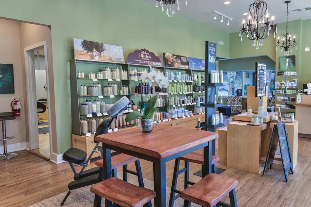 A salon interior with wooden furniture, shelves stocked with hair and skincare products, a massage chair, and a vase with white orchids on a central table. - Soleil 7 Hair Salon in Tallahassee, FL