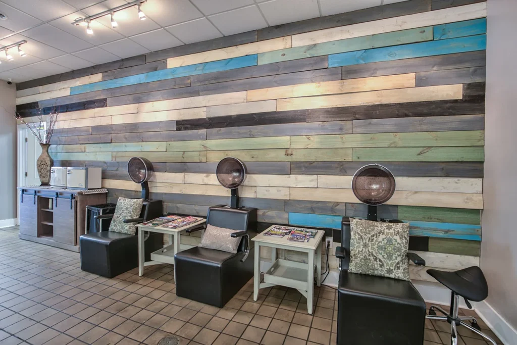 Salon waiting area with three black chairs and drying stations, colorful wooden plank accent wall, side tables with magazines, tile floor, and decorative vase in the corner. - Soleil 7 Hair Salon in Tallahassee, FL