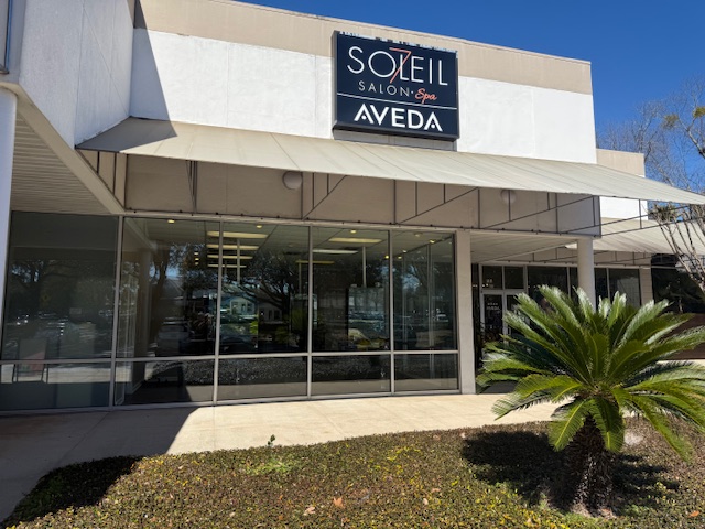 Exterior view of Soleil Salon & Spa Aveda with large windows, awning, and a small palm plant in front on a sunny day. - Soleil 7 Hair Salon in Tallahassee, FL
