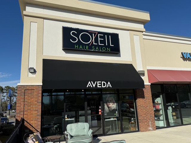 Exterior of Soleil Hair Salon with AVEDA branding, glass doors, and a poster in the window; chairs are placed outside on a sunny day. - Soleil 7 Hair Salon in Tallahassee, FL