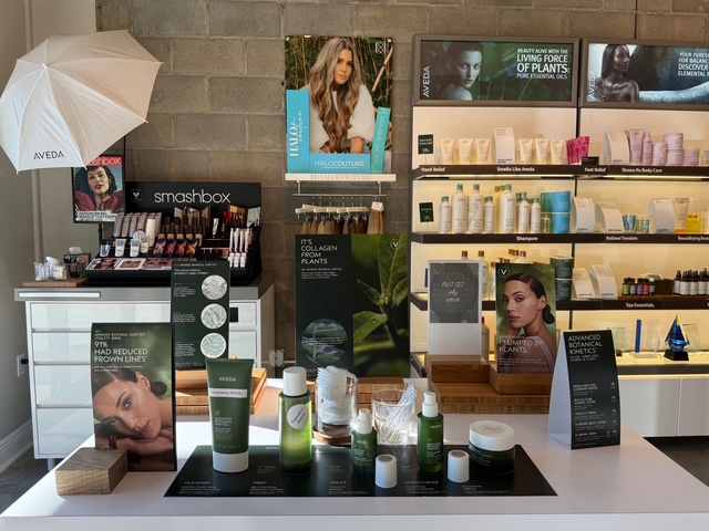 A retail display of skincare, haircare, and cosmetic products from brands like Aveda and Smashbox, with promotional posters and arranged product samples on shelves and counters. - Soleil 7 Hair Salon in Tallahassee, FL