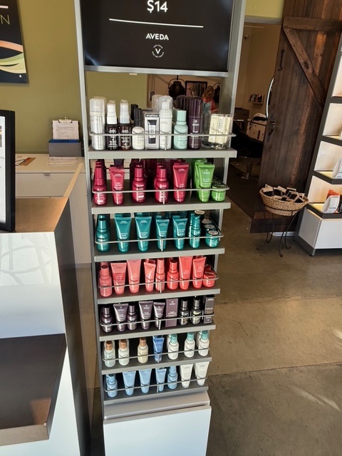Shelf display of assorted Aveda hair and skincare products arranged by color and type in a salon retail area. - Soleil 7 Hair Salon in Tallahassee, FL