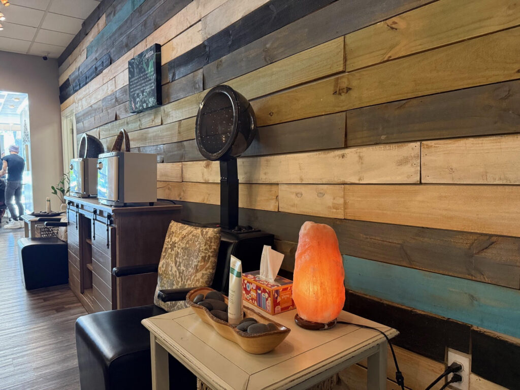 A cozy salon interior with wooden paneled walls, a salt lamp on a side table, a hair dryer chair, and salon equipment against the wall. - Soleil 7 Hair Salon in Tallahassee, FL